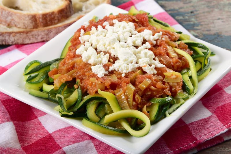 Plato de espaguetis de calabacín con salsa de tomate y cebolla dulce sobre un mantel de cuadros rojos y blancos