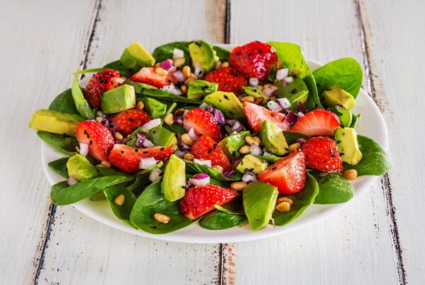 Plato de ensalada de espinacas con fresas y mango sobre una mesa de madera blanca