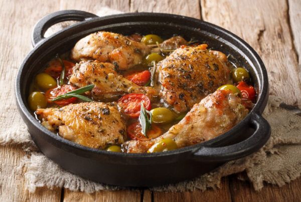 Cazuela de muslos de pollo con tomates cherry, aceitunas y cebolla dulce sobre una mesa de madera antigua