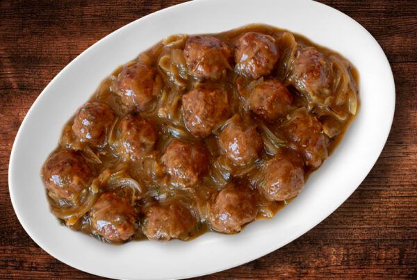 Fuente de albóndigas con queso y salsa de cebolla dulce sobre una mesa de roble