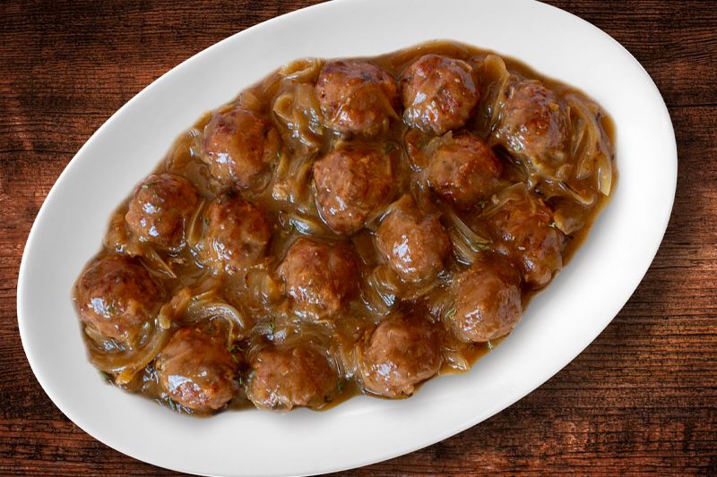 Fuente de albóndigas con queso y salsa de cebolla dulce sobre una mesa de roble