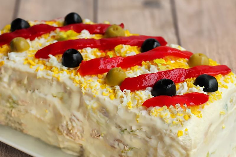 Pastel de patatas y atún sobre una fuente blanca decorado con tiras de pimiento rojo y aceitunas