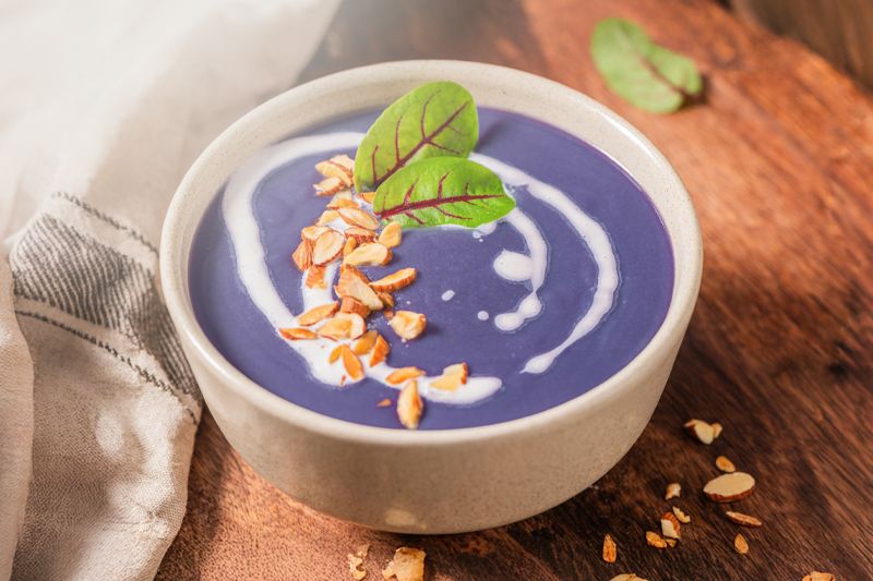 Cuenco blanco de crema de col lombarda sobre una mesa de madera oscura