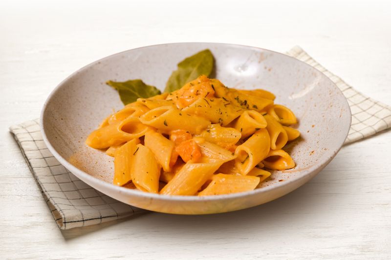 Plato de macarrones con salsa de calabaza y cebolla dulce sobre un paño de cocina en una mesa de madera clara casi blanca