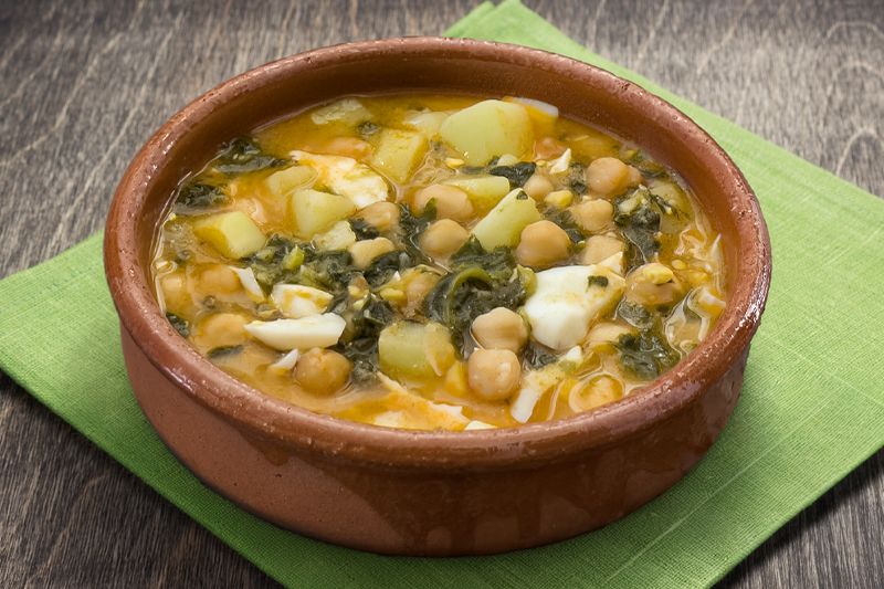Cazuela de potaje de garbanzos sobre una servilleta verde en una mesa de madera