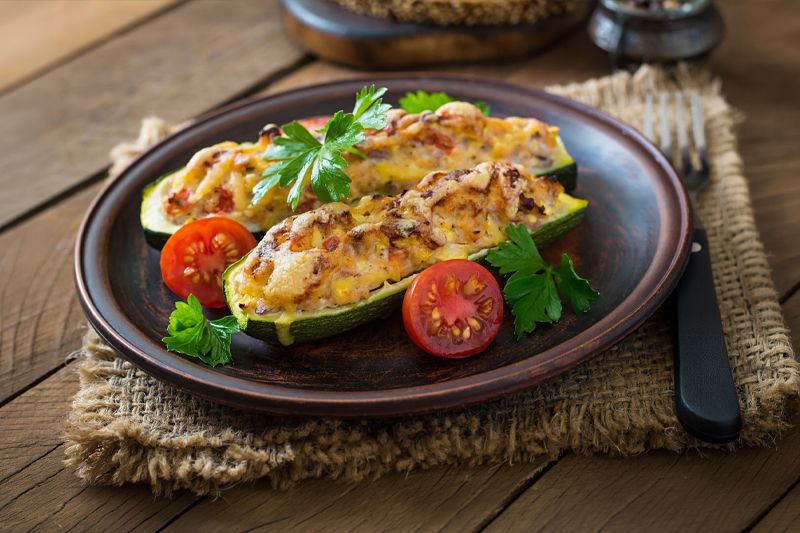Plato de calabacines rellenos de verduras, cebolla dulce y carne sobre una mesa de madera oscura