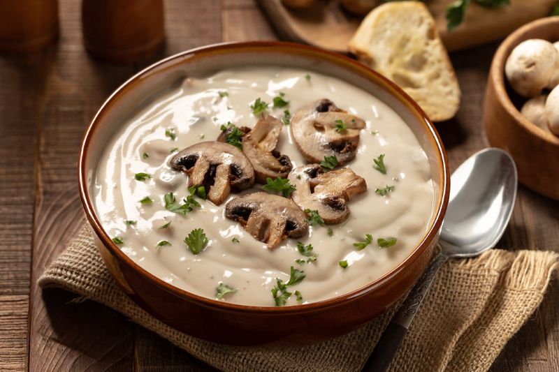 Plato de crema de champiñones sobre una servilleta de arpillera en una mesa de madera oscura.