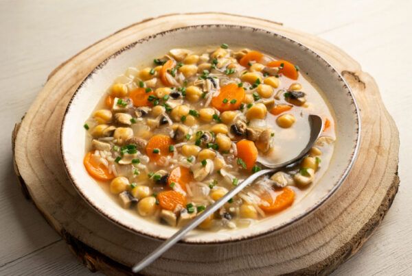 Plato de sopa de garbanzos con arroz con una cuchara dentro sobre una tabla redonda de madera