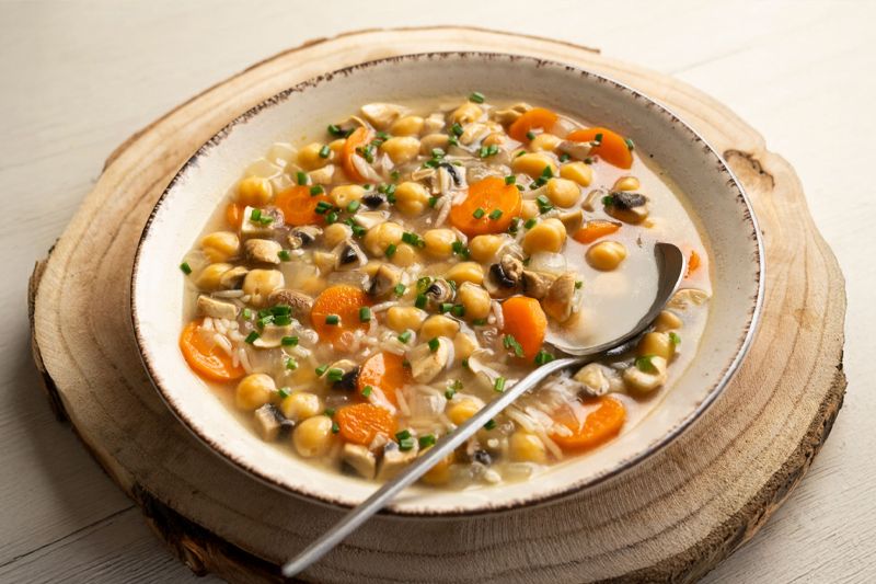 Plato de sopa de garbanzos con arroz con una cuchara dentro sobre una tabla redonda de madera