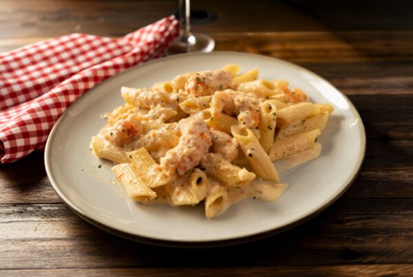 Plato de pasta con salsa de cebolla dulce y gambones sobre una mesa de madera oscura