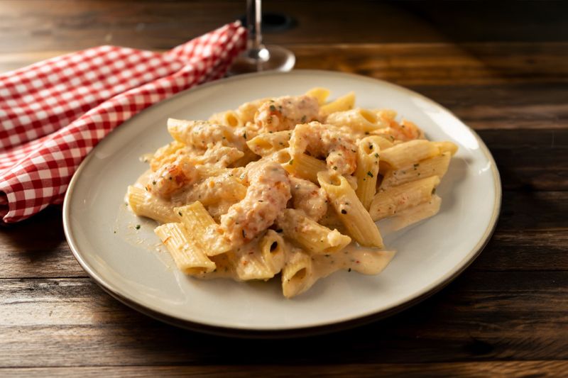 Plato de pasta con salsa de cebolla dulce y gambones sobre una mesa de madera oscura