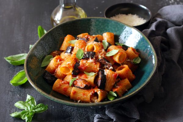 Plato de pasta de lentejas rojas con berenjenas y salsa de tomate con cebolla dulce Consuay sobre una mesa de madera pintada en gris oscuro