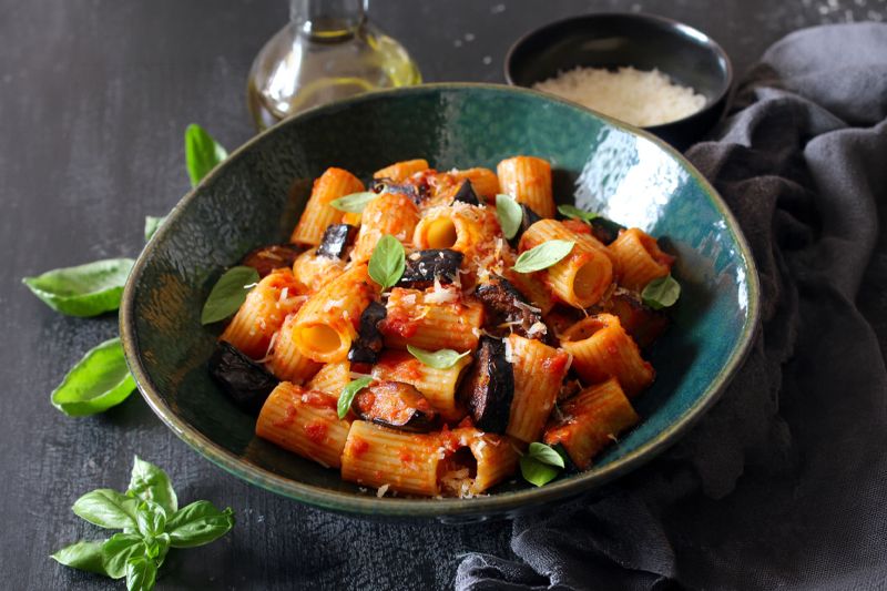 Plato de pasta de lentejas rojas con berenjenas y salsa de tomate con cebolla dulce Consuay sobre una mesa de madera pintada en gris oscuro