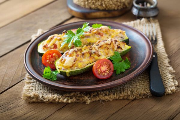 Calabacines rellenos de atún con cebolla dulce, huevo, tomate y queso rayado presentado en un plato de barro marrón, encima de un mantel individual de pita en una mesa de madera oscura.