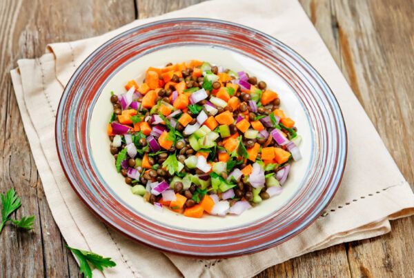 Plato de ensalada de lentejas, zanahorias, cebolla dulce y apio sobre una servilleta en una mesa de madera.